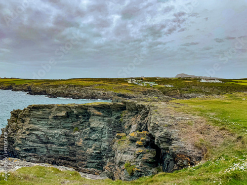 A breathtaking view of Anglesey's rugged cliffs, towering over the crashing waves of the Irish Sea. The vibrant green grass contrasts beautifully with the deep blue waters. photo