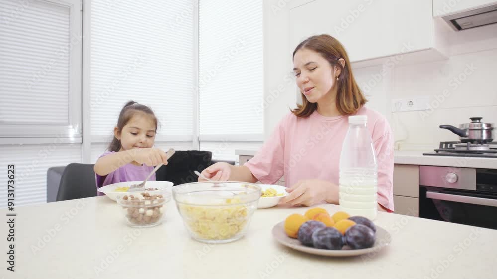A loving mother serves cereal with milk to her happy daughter for breakfast, creating a joyful moment as they eat, chat and laugh together. A loving mother serves cereal with milk to her happy daughter for breakfast, creating a joyful moment as they eat, chat and laugh together.