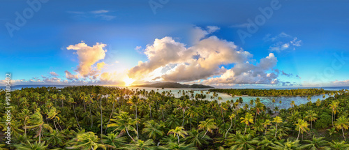 Panoramic view of beautiful tropical jungle filled with green palm trees on a motu near the French Polynesia island of Taha'a. Vibrant turquoise blue south pacific ocean water surrounds the white sand