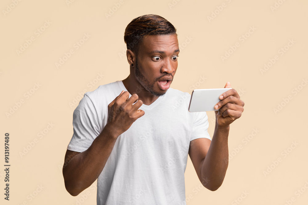 Shocking News. Amazed Afro Guy Looking At Smartphone Reading Message Standing Over Yellow Background In Studio Shocking News. Amazed Afro Guy Looking At Smartphone Reading Message Standing Over Yellow Background In Studio