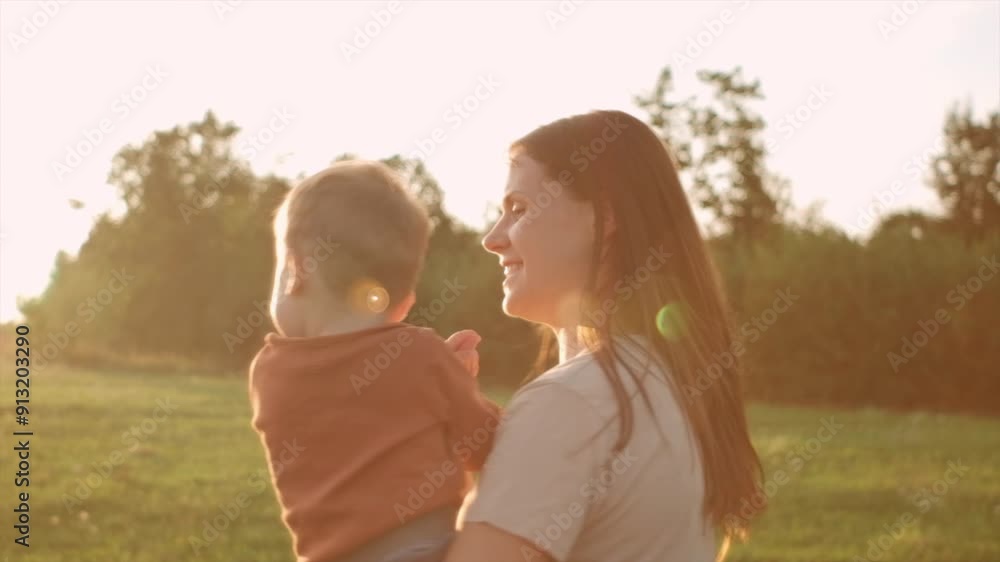 Cheerful young mother and cute baby son enjoying summer nature during warm sunset. Playful happy mom and toddler boy playing on field at summertime. Family having fun together. Slow-motion Cheerful young mother and cute baby son enjoying summer nature during warm sunset. Playful happy mom and toddler boy playing on field at summertime. Family having fun together. Slow-motion