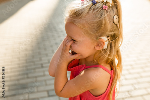 Funny baby with cochlear implant walks outdoor. Hearing aid and medicine innovating technology concept. Diversity and inclusion and people with disability concept. Copy space