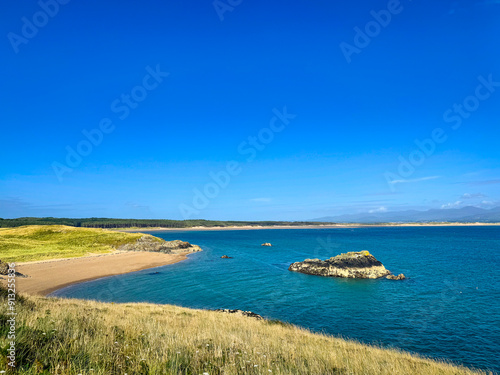 A serene beach in Anglesey, encircled by majestic cliffs, where golden sands meet turquoise waters under a vast, clear sky. Perfect natural beauty.