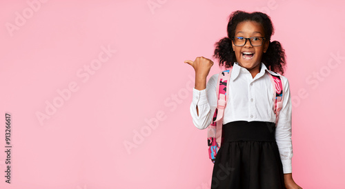 Look There. Excited Afro Elementary Student Girl Pointing Thumbs At Copy Space Over Yellow Studio Background. Panorama photo