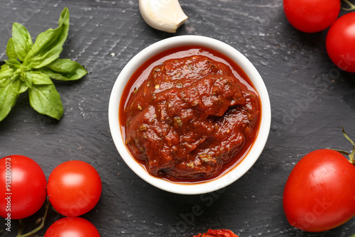 Composition with bowl of delicious tomato sauce and ingredients on black wooden table