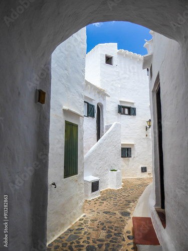 Charming alley in Binibeca village, Menorca, with white stone houses and colorful wooden windows and doors. Idyllic summer day with sunshine.