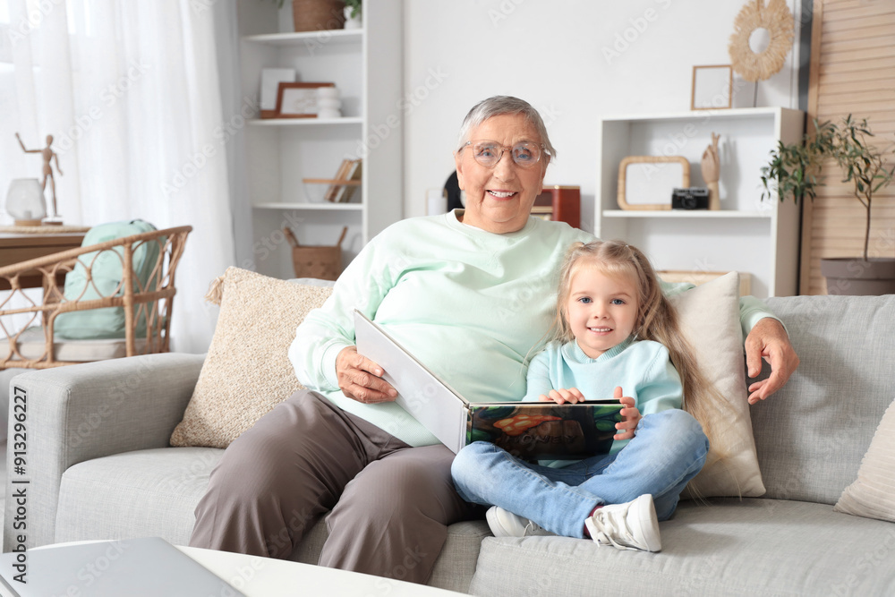 Cute little girl with her granny reading story on sofa at home Cute little girl with her granny reading story on sofa at home