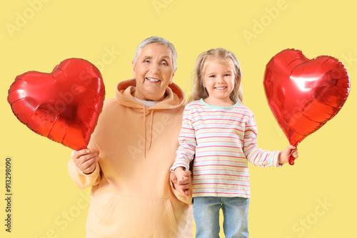 Canvas Print Cute little girl with her granny and heart-shaped balloons on yellow background