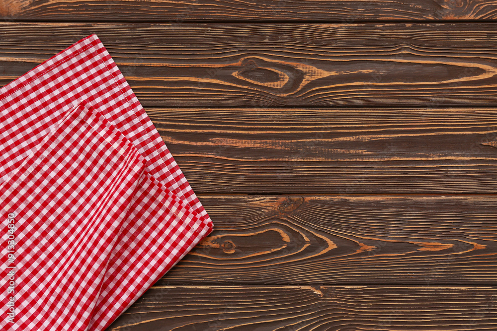 Obraz premium Red and white gingham checkered fabric napkin on dark brown rustic wooden table background, the textile provides a classic country or farmhouse aesthetic for dining and kitchen concepts