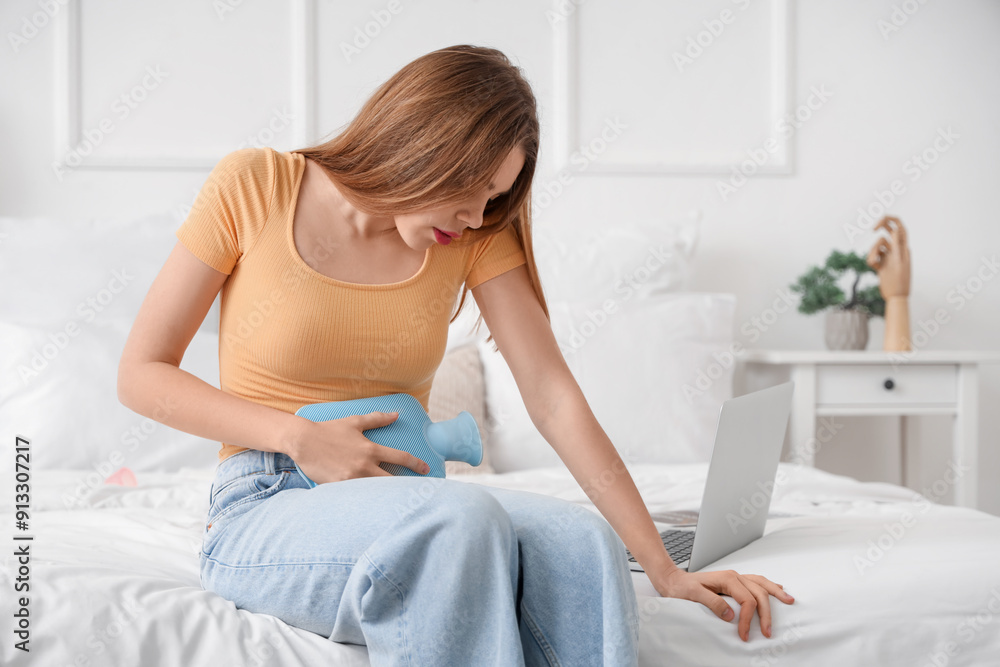 Young woman suffering from menstrual cramps with hot water bottle in bedroom Young woman suffering from menstrual cramps with hot water bottle in bedroom