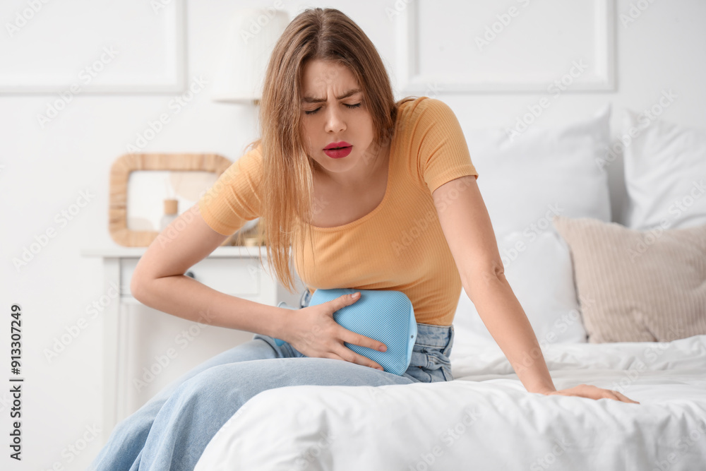 Young woman with hot water bottle suffering from menstrual cramps in bedroom Young woman with hot water bottle suffering from menstrual cramps in bedroom