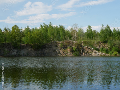 Small waves on the water against the background of a stone quarry covered with trees