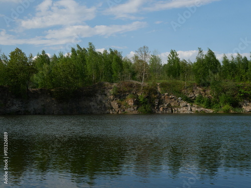 Small waves on the water against the background of a stone quarry covered with trees