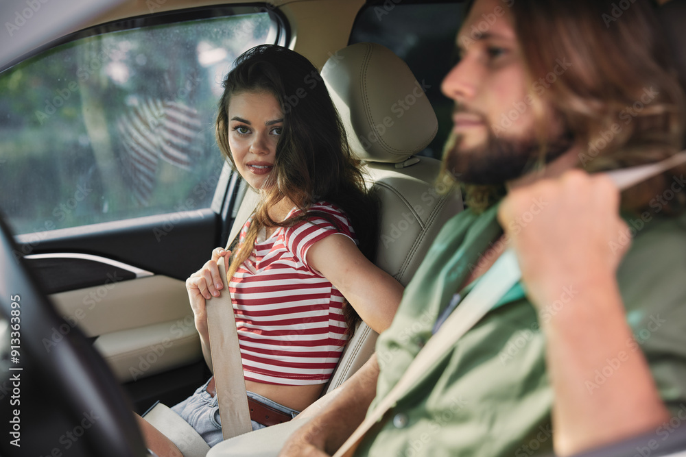 A young couple inside a car, the woman fastening her seatbelt while the man looks ahead, both focused on the road A young couple inside a car, the woman fastening her seatbelt while the man looks ahead, both focused on the road