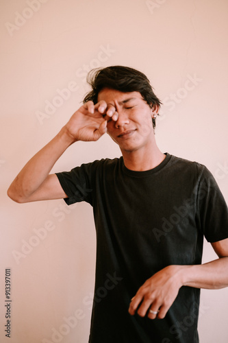 A Southeast Asian man rubbing his eyes due to itchiness, capturing a moment of irritation or discomfort, perfect for health, lifestyle