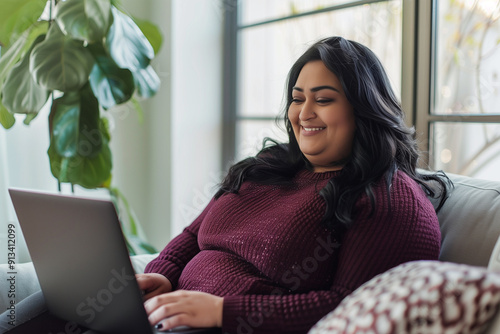 An overweight Hindu businesswoman sitting in an office using a computer, smiling.