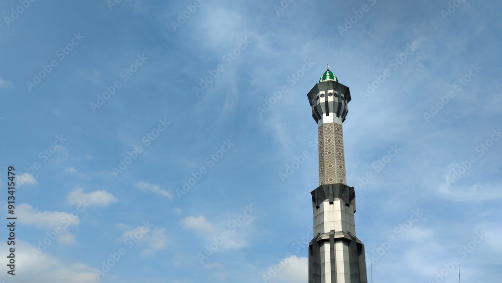 A low-angle view of mosque tower against a blue sky with wispy clouds. A low-angle view of mosque tower against a blue sky with wispy clouds.