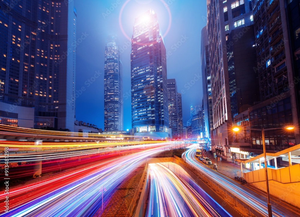 A night scene of a Hong Kong street with tall buildings and brightly lit windows. Light trails from cars moving along the street create a colorful and dynamic scene. A night scene of a Hong Kong street with tall buildings and brightly lit windows. Light trails from cars moving along the street create a colorful and dynamic scene.