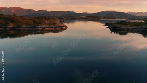 Flight over the mirrorlike ocean, rocky archipelago, and scattered fishing villages. The setting sun fills the scene with a warm glow. photo