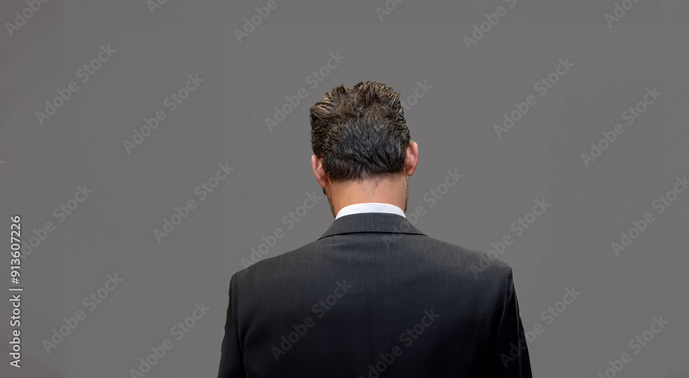 Back of young businessman in a grey suit against a gray background with negative space on the left and right Back of young businessman in a grey suit against a gray background with negative space on the left and right