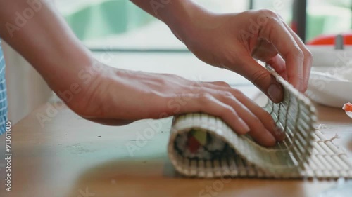 A person is making a sushi roll with a piece of avocado