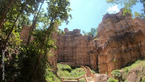 A rocky canyon with a wooden bridge leading to a lush green forest. The bridge is surrounded by trees and rocks, creating a serene and peaceful atmosphere photo