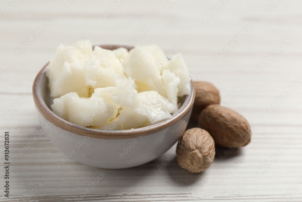 Shea butter in bowl and nuts on white wooden table, closeup Shea butter in bowl and nuts on white wooden table, closeup