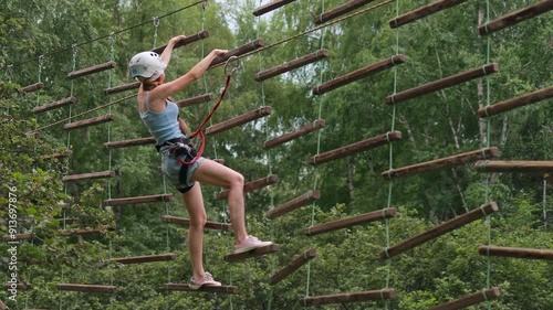 Rope park, entertainment and sports, close-up of a woman in a safety harness and helmet, view from the back, overcomes an obstacle course made of wood at a height