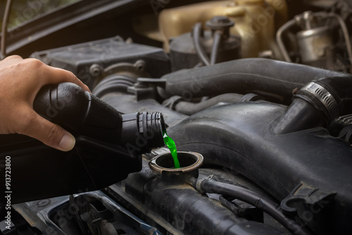 Mechanician hand filling pre-mixed green coolant into the radiator and car cooling system. Background for cars maintenance with selective focus and copy space.