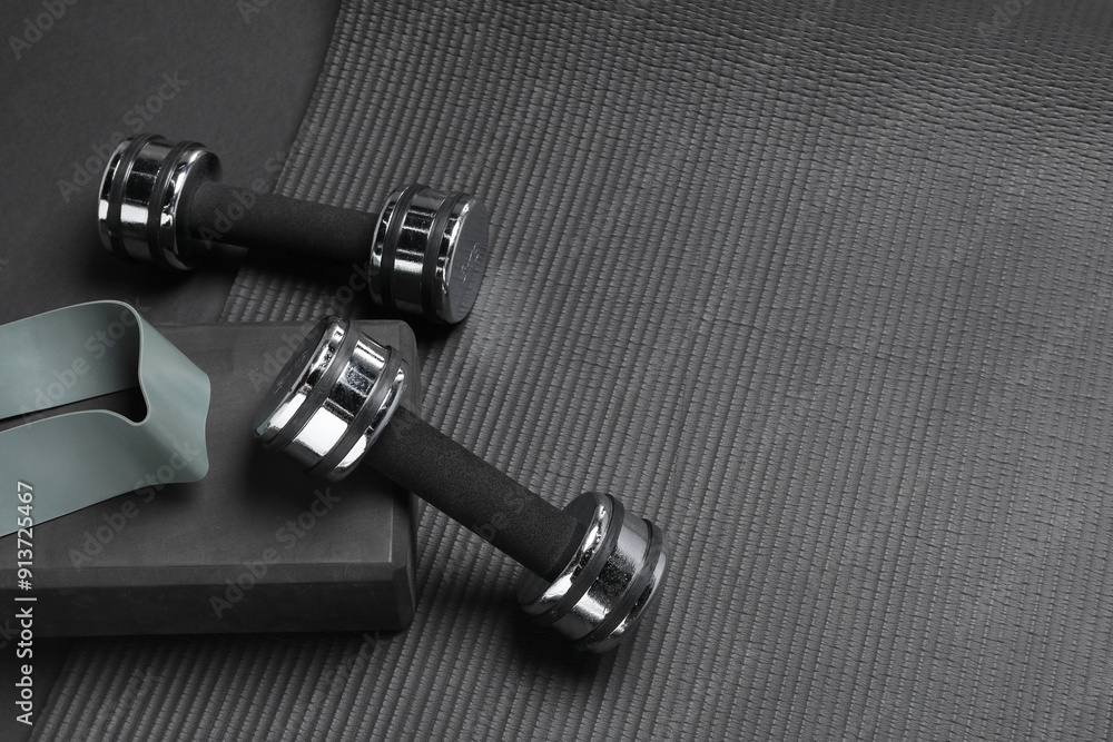 Dumbbells, yoga block, mat and fitness elastic band on black background, above view. Space for text Dumbbells, yoga block, mat and fitness elastic band on black background, above view. Space for text