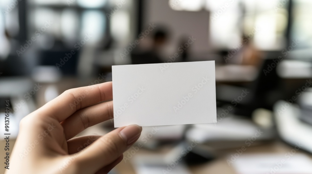 A hand offers a blank white business card in a bright office, highlighting professional networking and opportunities in a contemporary workspace A hand offers a blank white business card in a bright office, highlighting professional networking and opportunities in a contemporary workspace