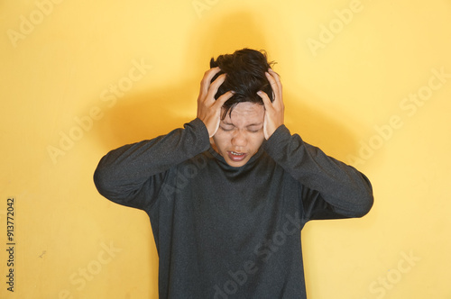 young asian man showing pain expression while touching head with his hand