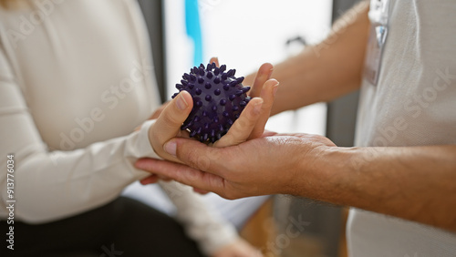 Принти на полотні A woman therapist assists a man patient with a spiky purple massage ball in a bright rehabilitation center