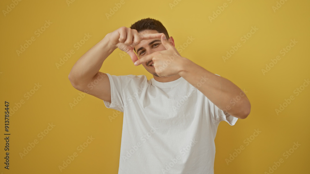 Young man with beard framing face with fingers against yellow background Young man with beard framing face with fingers against yellow background