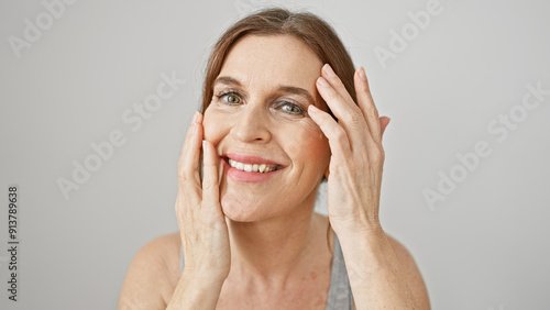 A cheerful, middle-aged woman touches her face, posing against a white background with a beaming smile.