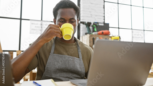 A young african american man drinking coffee during a break in a well-equipped carpentry workshop. photo