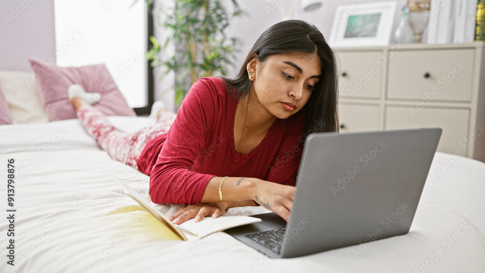 Young, south asian woman in casual attire working on a laptop while lying on a bed in a well-lit bedroom. Young, south asian woman in casual attire working on a laptop while lying on a bed in a well-lit bedroom.