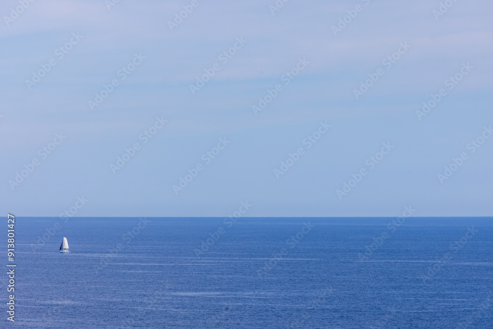 Photo of a sail boat out in the ocean on a clear blue sky day taken in the city of Benidorm in Spain on a sunny day in the summer time Photo of a sail boat out in the ocean on a clear blue sky day taken in the city of Benidorm in Spain on a sunny day in the summer time