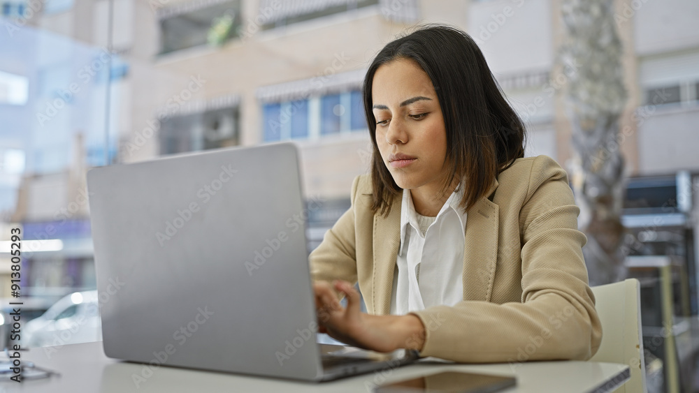 Focused young woman using a laptop at a modern workplace, displaying professionalism and seriousness Focused young woman using a laptop at a modern workplace, displaying professionalism and seriousness