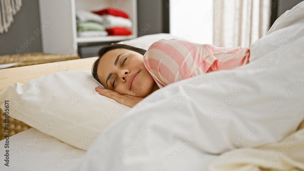 A serene hispanic woman peacefully sleeping in a cozy bedroom with white bedding and a striped pajama. A serene hispanic woman peacefully sleeping in a cozy bedroom with white bedding and a striped pajama.