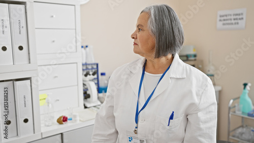 Mature woman scientist in lab coat with id badge stands thoughtfully in medical laboratory. photo