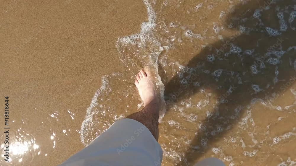Pies de hombre caucásico andando sobre la fina arena de la playa de Tazones y bañado por las aguas del litoral Cantábrico, norte de España