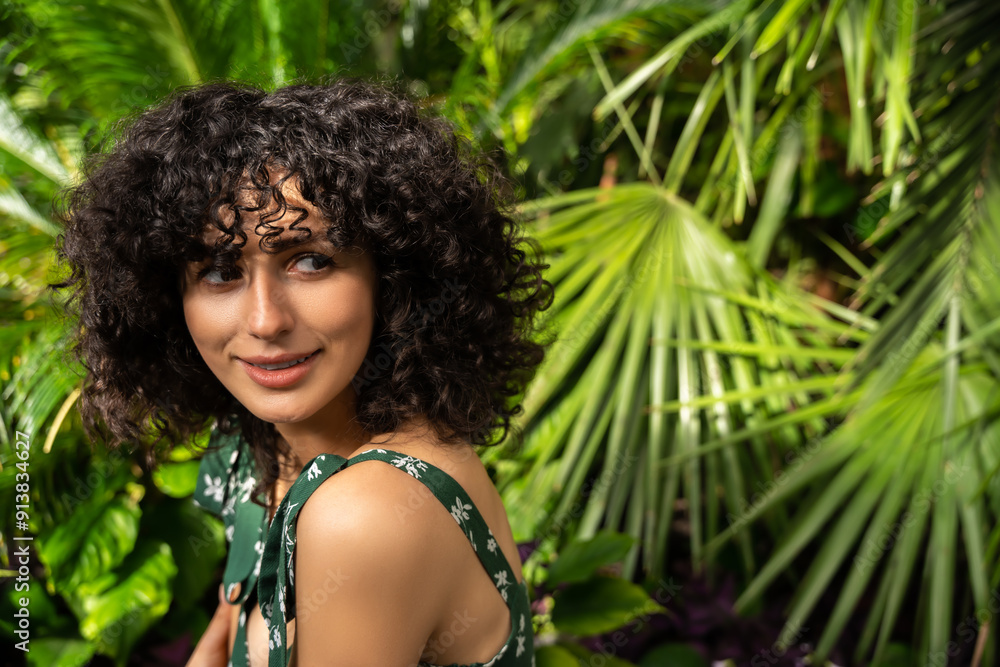 Woman with curly hair on a background of tropical leaves indoor Woman with curly hair on a background of tropical leaves indoor