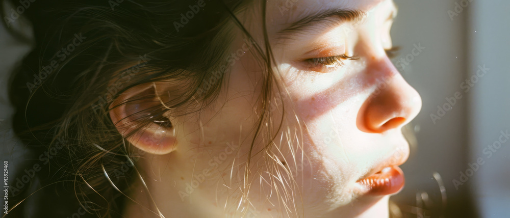 Sunlight casts soft shadows across a woman's serene face, capturing a peaceful, introspective moment. Sunlight casts soft shadows across a woman's serene face, capturing a peaceful, introspective moment.