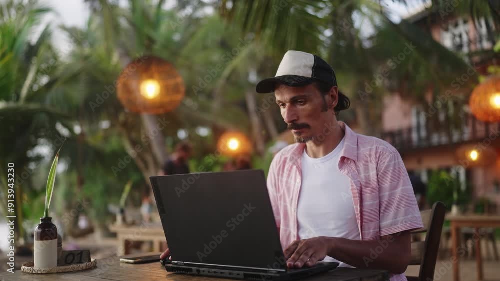 Focused man works on laptop at beach cafe during sunset. Remote worker finishes project near ocean. Freelancer types, surrounded by tropical scenery. Digital nomad lifestyle captured at dusk. Slowmo Focused man works on laptop at beach cafe during sunset. Remote worker finishes project near ocean. Freelancer types, surrounded by tropical scenery. Digital nomad lifestyle captured at dusk. Slowmo