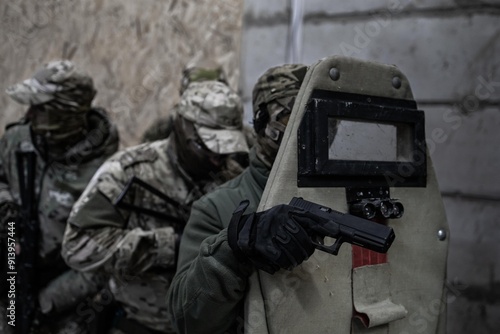 Φωτογραφία A group of military men in camouflage lined up behind a soldier with an armored shield and a pistol against a concrete wall