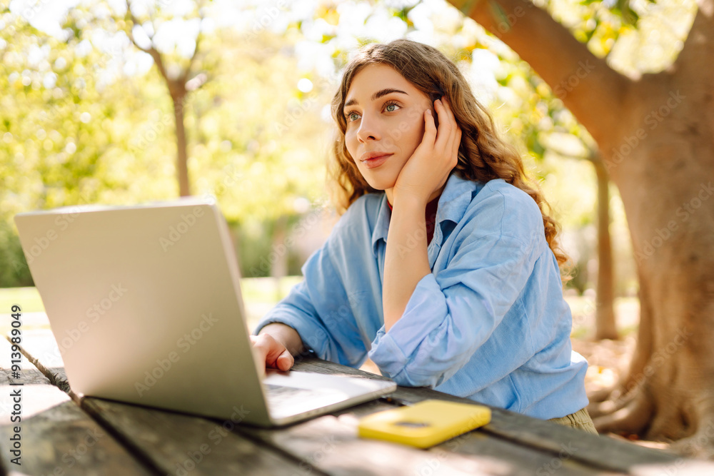 Female student typing on laptop sitting near university building, Education and modern technologies. Female student typing on laptop sitting near university building, Education and modern technologies.