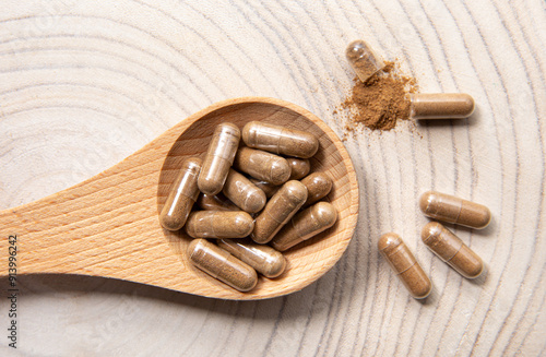 Withania somnifera known as ashwagandha. Ashwagandha root powder supplement capsules on wood spoon, studio shot.