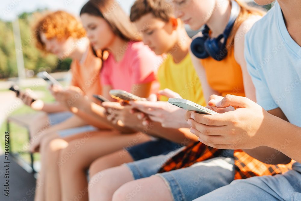 Cheerful children using mobile phones sitting in a row on bench in the city Cheerful children using mobile phones sitting in a row on bench in the city