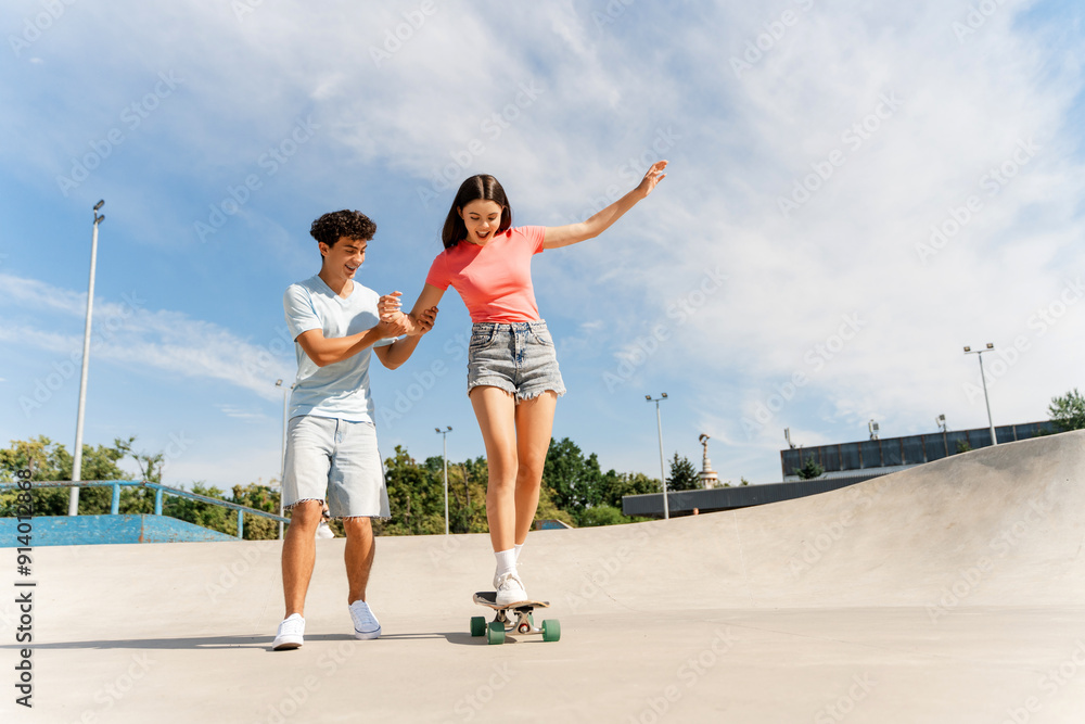 Fototapeta premium Happy teenage couple riding short modern skateboards at the skate park